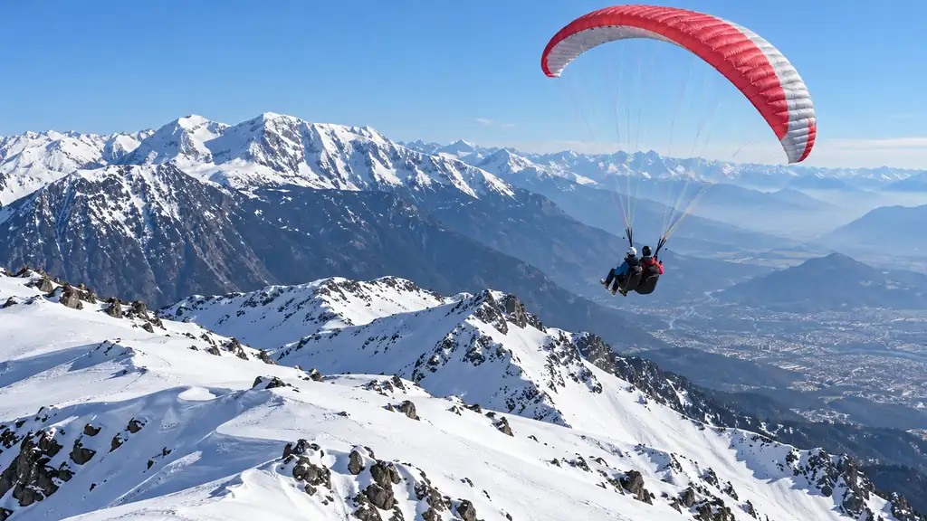 Parapente biplace au-dessus de reliefs enneigés de Belledonne.